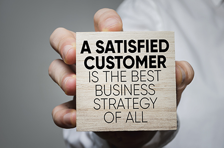 A hand holding a block that says " A SATISFIED CUSTOMER IS THE BEST BUSINESS STRATEGY OF ALL"