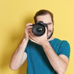 Professional Lavallette real estate photographer with camera up to their eye in front of a yellow background